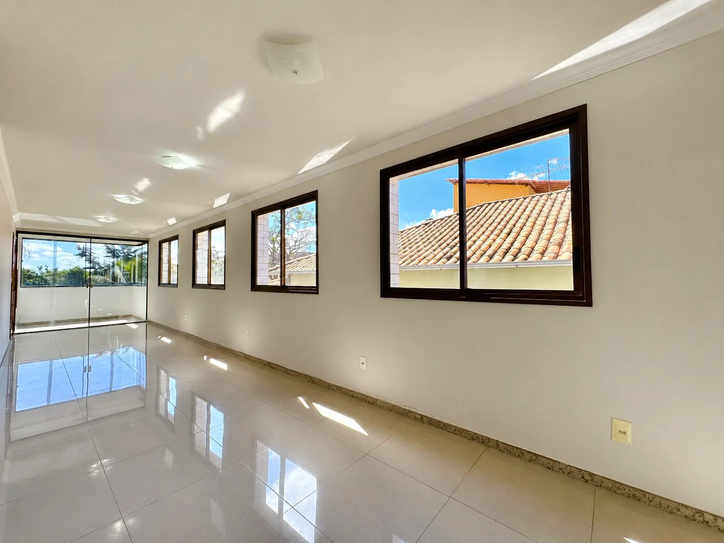 Sala panorâmica com cinco janelas, piso polido brilhante e acesso à varanda